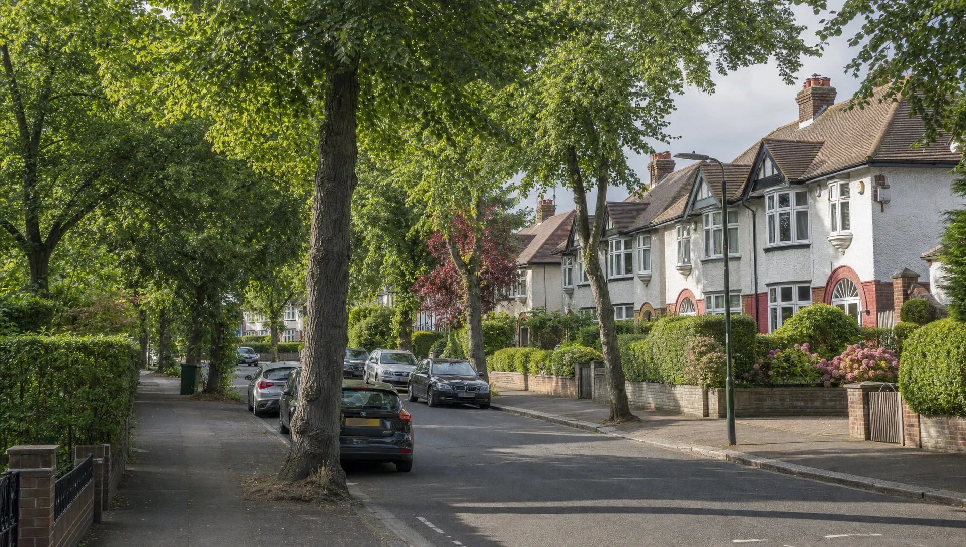 A quiet tree-lined Uxbridge street with 1930s semi-detached houses, neat front gardens and parked cars.